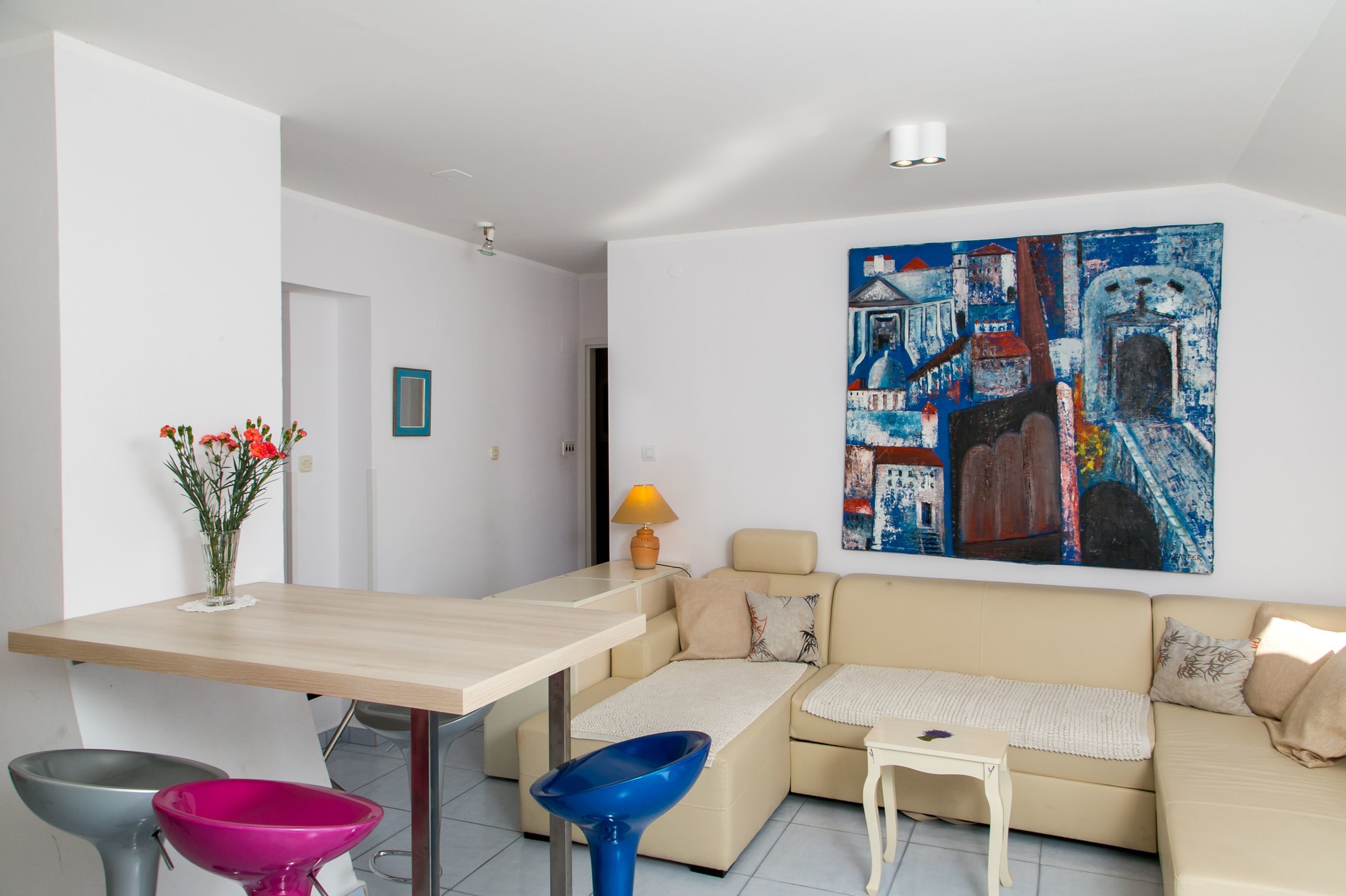 Un salon moderne avec un canapé beige, une table basse en bois et un tableau abstrait aux couleurs vives accroché au mur.