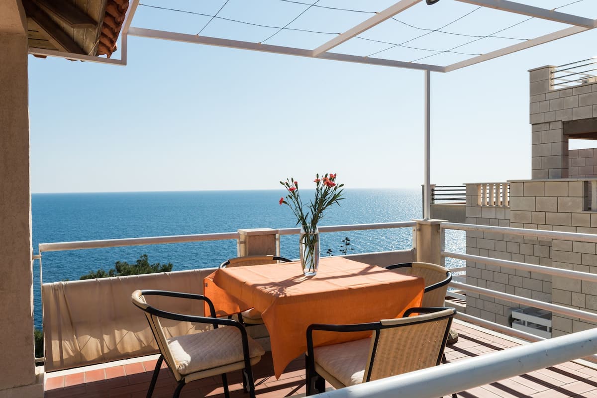 Uma varanda com mesa e cadeiras, com vista para o mar.