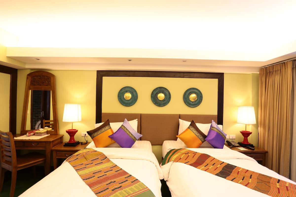 A hotel room with two beds, a desk, and a chair. There are lamps on either side of the beds and a mirror above the desk.