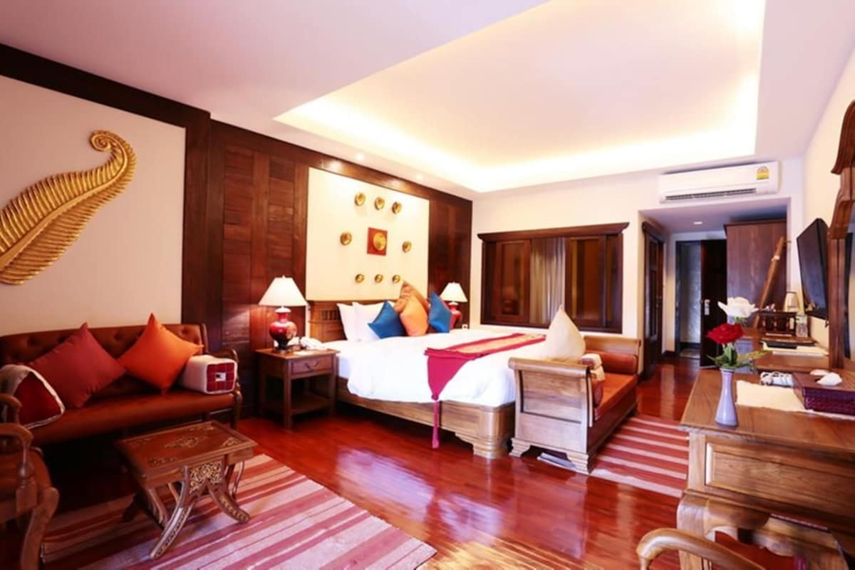 A hotel room with a large bed, a sofa, a wooden coffee table, and a desk with a chair.