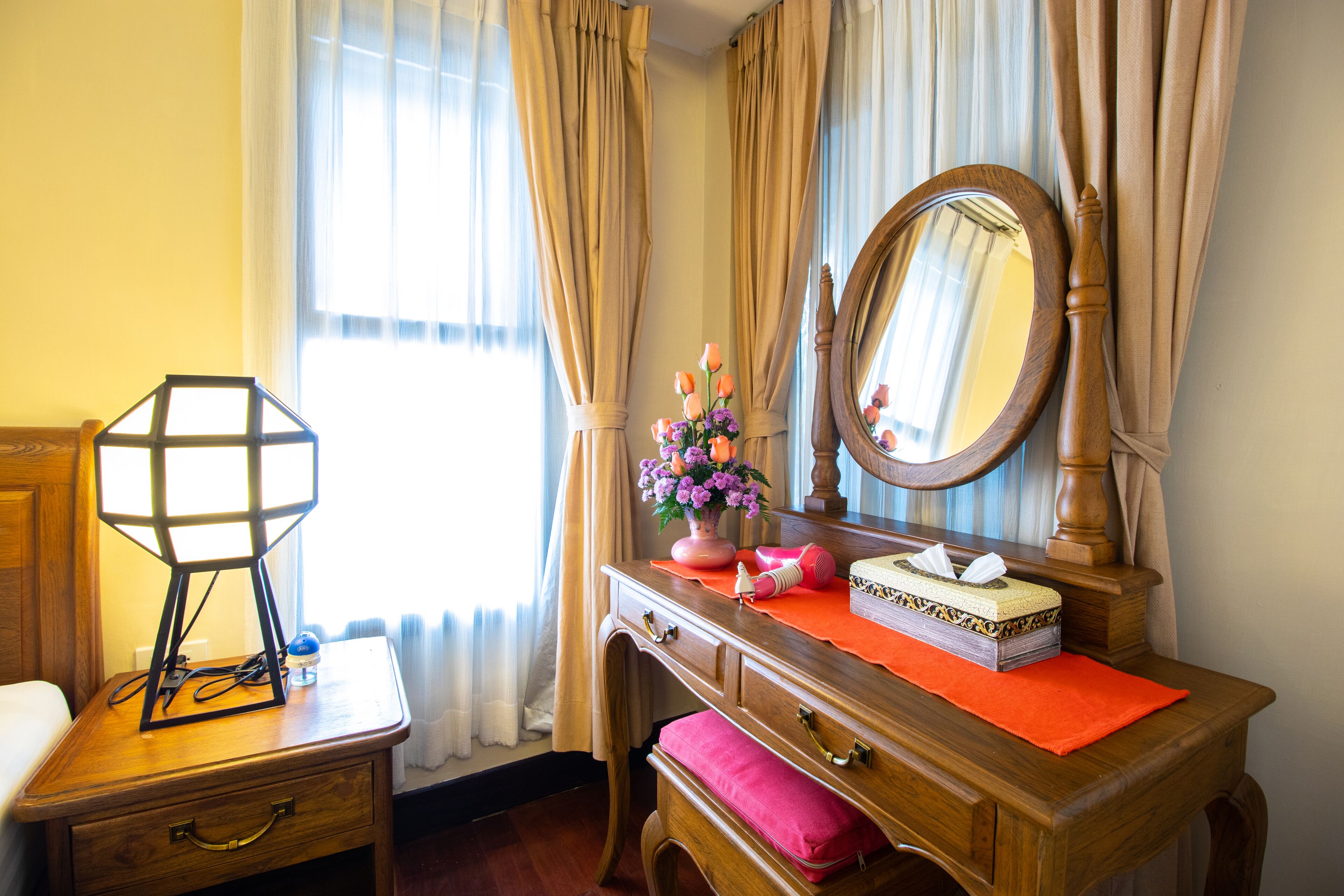 A wooden dresser with a mirror, a vase with flowers, and a tissue box.