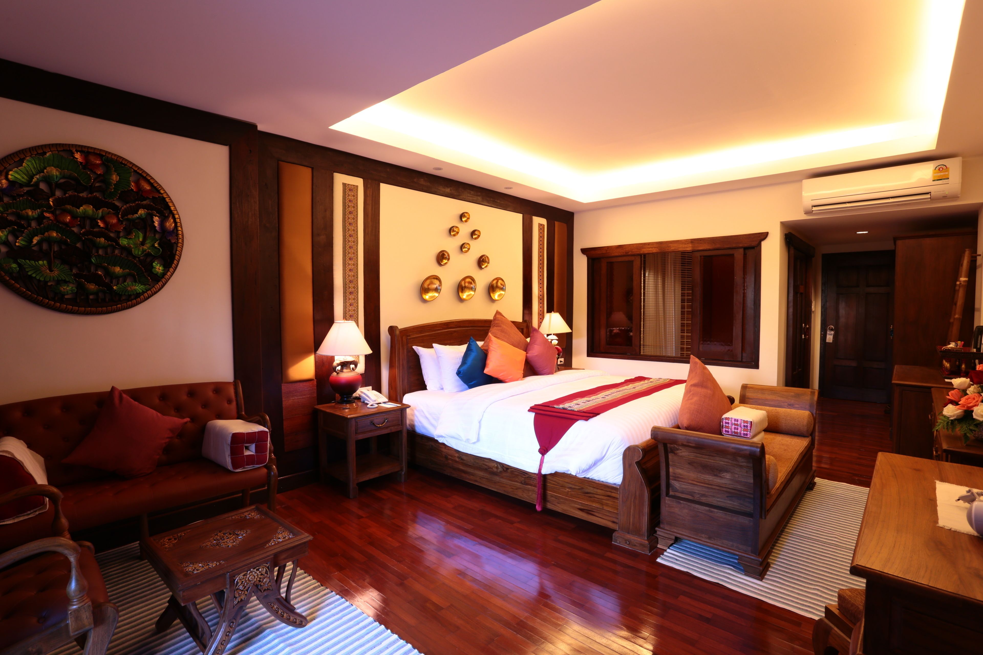A hotel room with a large bed, a sofa, a wooden coffee table, and a nightstand with a lamp.