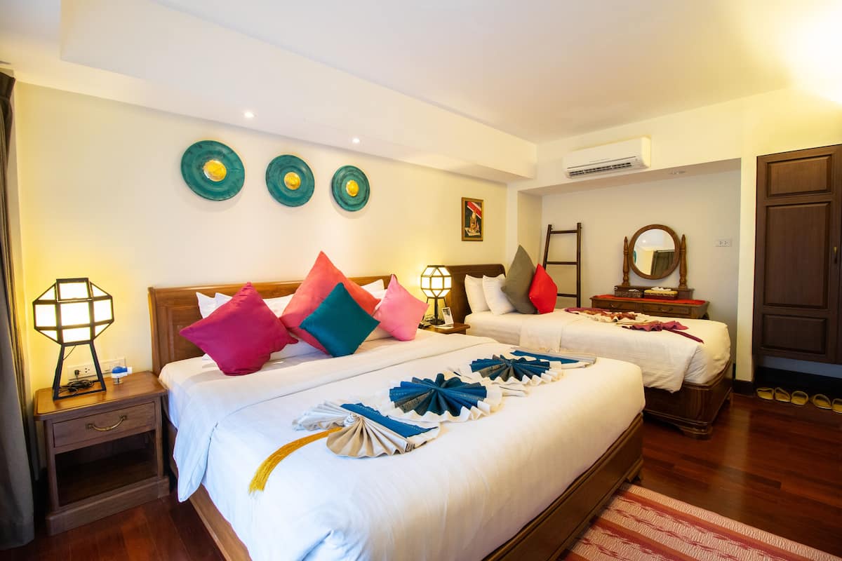 A hotel room with two beds, a nightstand, a lamp, a mirror, and a wooden wardrobe.