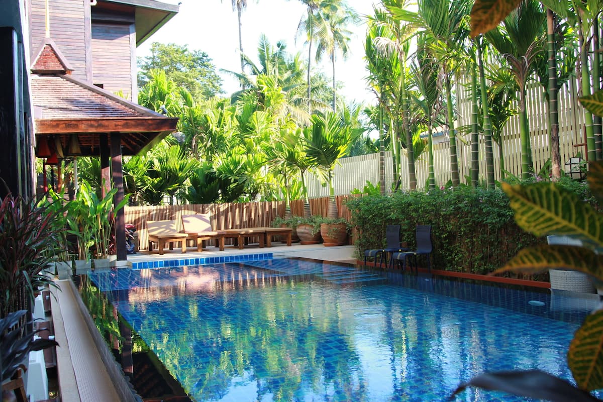 A swimming pool with a wooden deck, lounge chairs, and a bamboo fence.