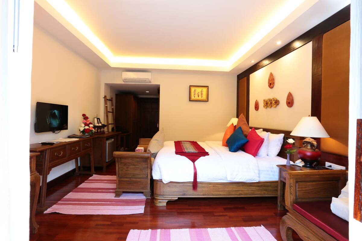 A hotel room with a wooden bed, a desk, a television, and a lamp.