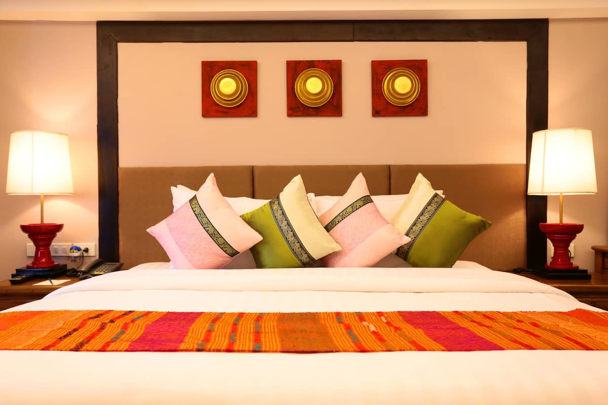 A hotel room with a large bed, multiple pillows, two bedside lamps, and three wall-mounted artworks.