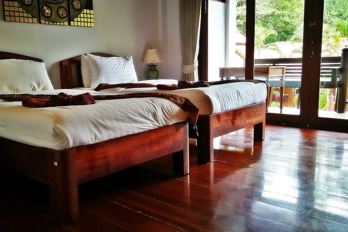 A wooden bed with white linens, a nightstand, a lamp, and a view of the outdoors.