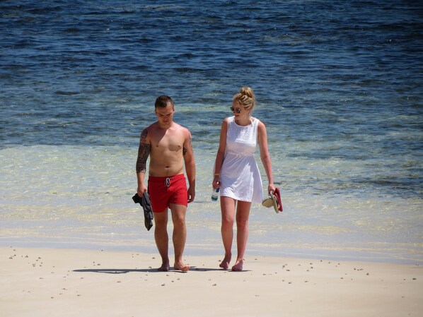 Two people walking on a beach with clear water in the background.