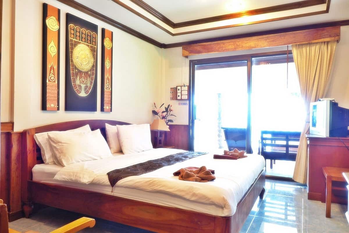 A hotel room with a wooden bed, a TV, a balcony, and decorative wall art.