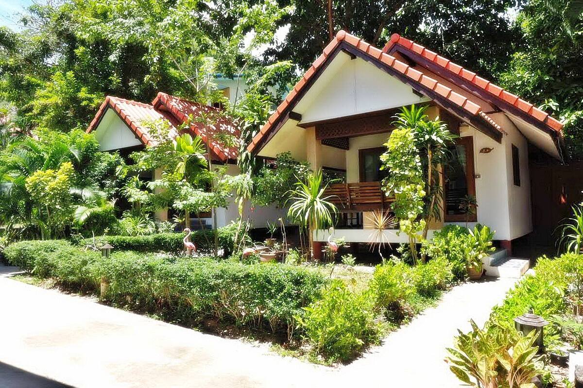 Ein Bungalow mit rotem Ziegeldach, umgeben von üppiger Vegetation und einem gepflegten Garten.