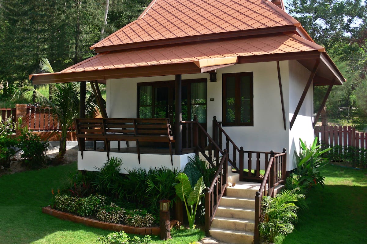 Ein zweistöckiges Haus mit rotem Ziegeldach, einer Holzveranda und einer Treppe, die zum Eingang führt.