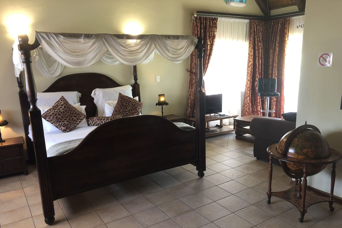 Ein Hotelzimmer mit einem Himmelsbett, einem Blätterdach, einem Fernseher, einem Globus und einem Schreibtisch mit Stuhl.