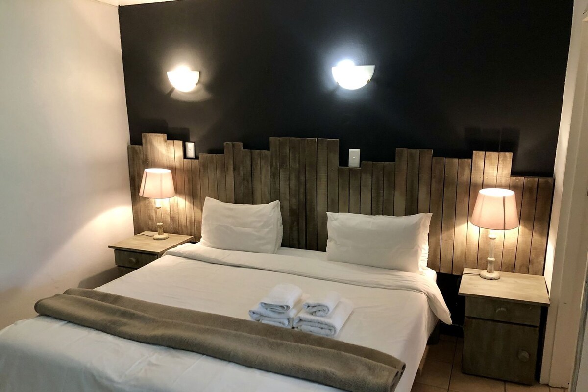 Een hotelkamer met een groot bed, twee nachtkastjes met lampen, een houten hoofdbord en een bijzettafeltje met een lamp.