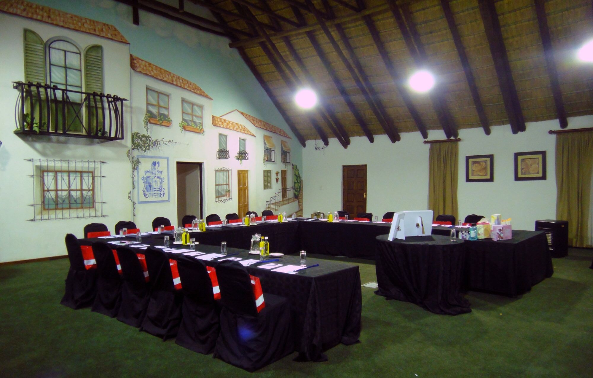 Un salón de conferencias con largas mesas, sillas y un techo alto con vigas de madera.