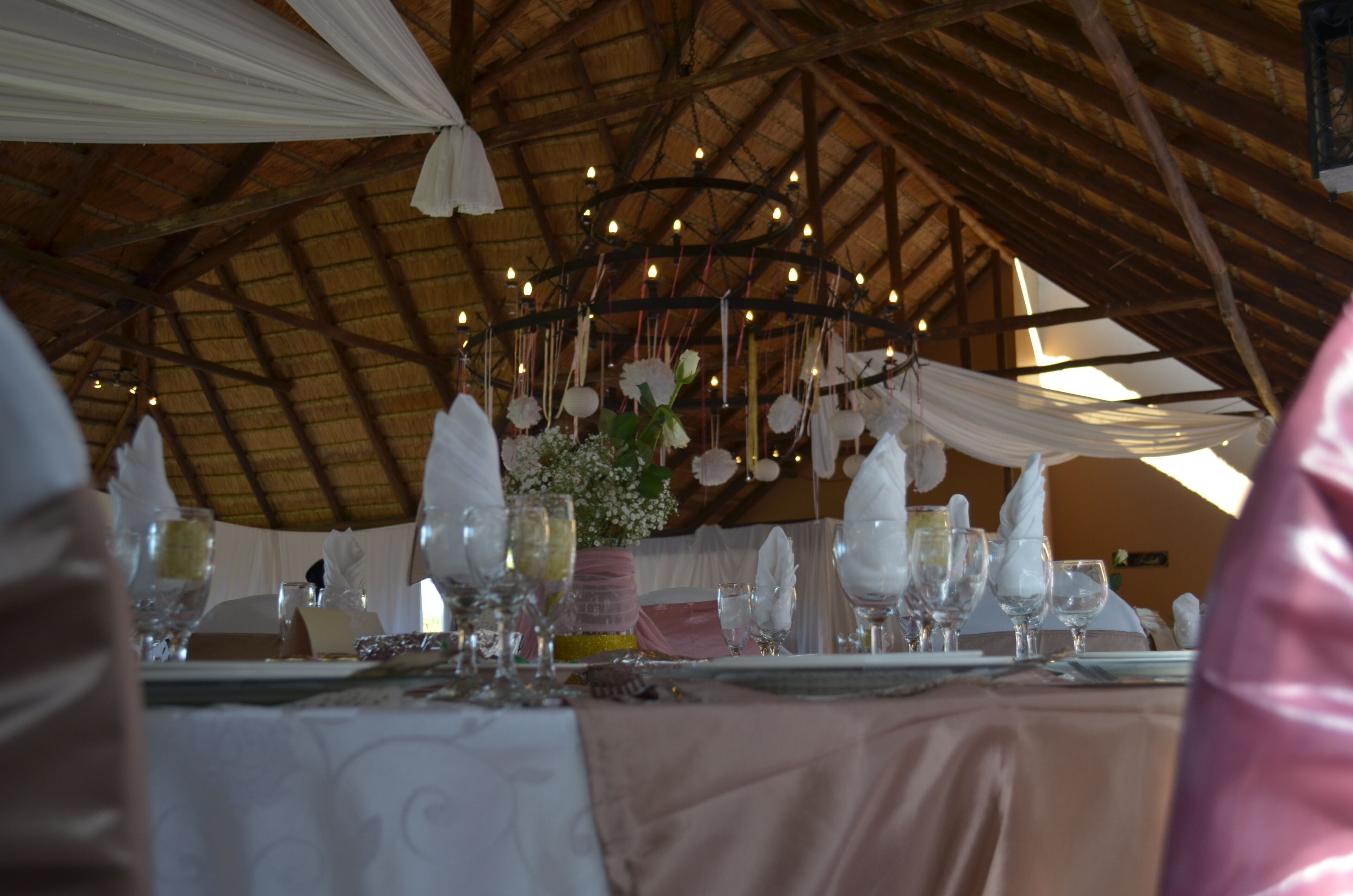 Un salón de banquetes con techo alto y vigas de madera, decorado con luces colgantes y telas drapeadas.