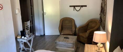 A hotel room with a bed, two wicker chairs, a small table, a lamp, and a door leading to a closet.