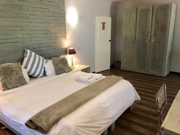 A neatly made bed with pillows and a blanket, a bedside lamp, a wooden wardrobe, and a door with a sign. - Valverde Country Hotel (Muldersdrift)