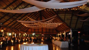 An indoor venue with round tables covered in white tablecloths, wooden beams on the ceiling, and string lights. - Valverde Country Hotel (Muldersdrift)
