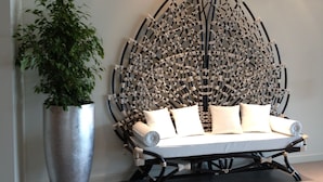 Una habitación moderna con una original instalación artística en la pared, una planta grande en maceta y un sofá minimalista con cojines.