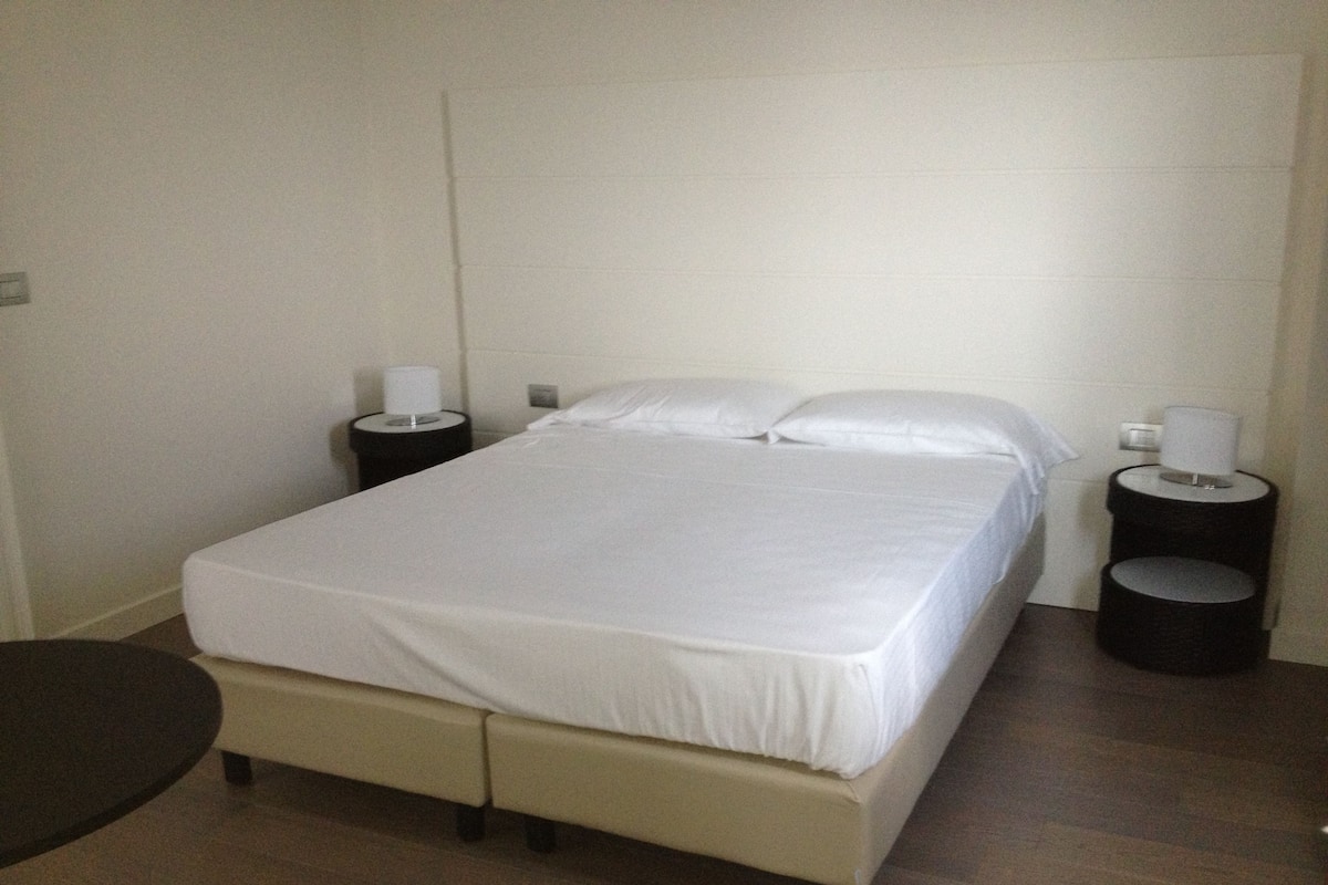 A single bed with a white mattress and pillows, flanked by two black nightstands with lamps.
