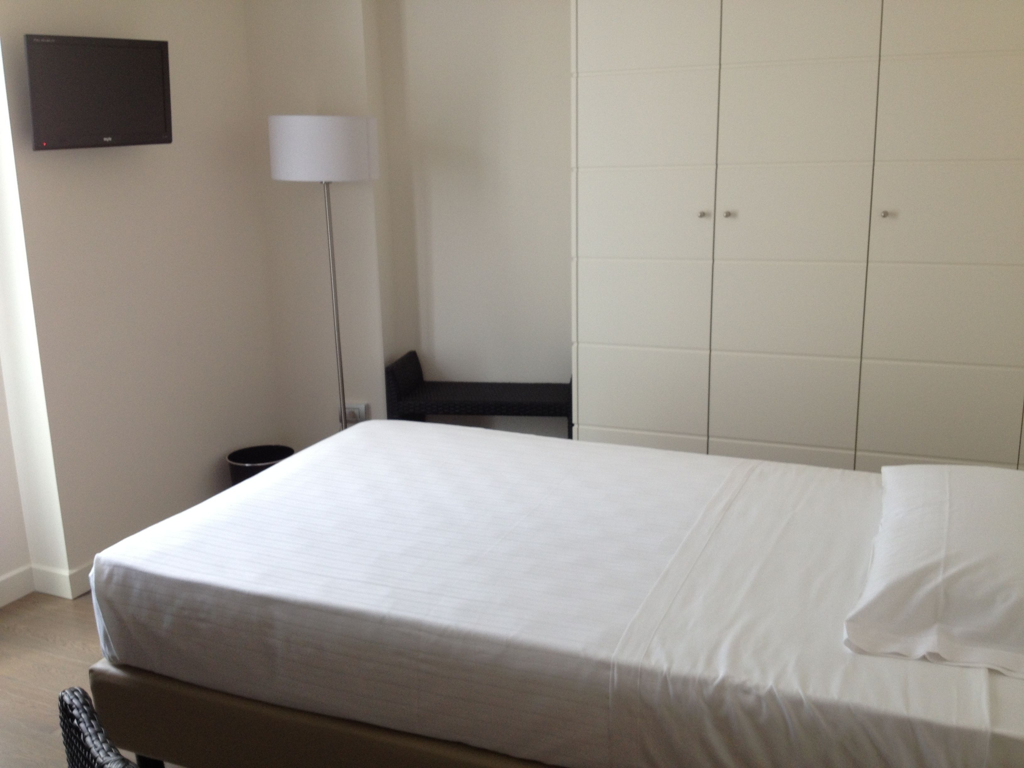 Una habitación de hotel con una cama, una mesita de noche, una lámpara y un armario.