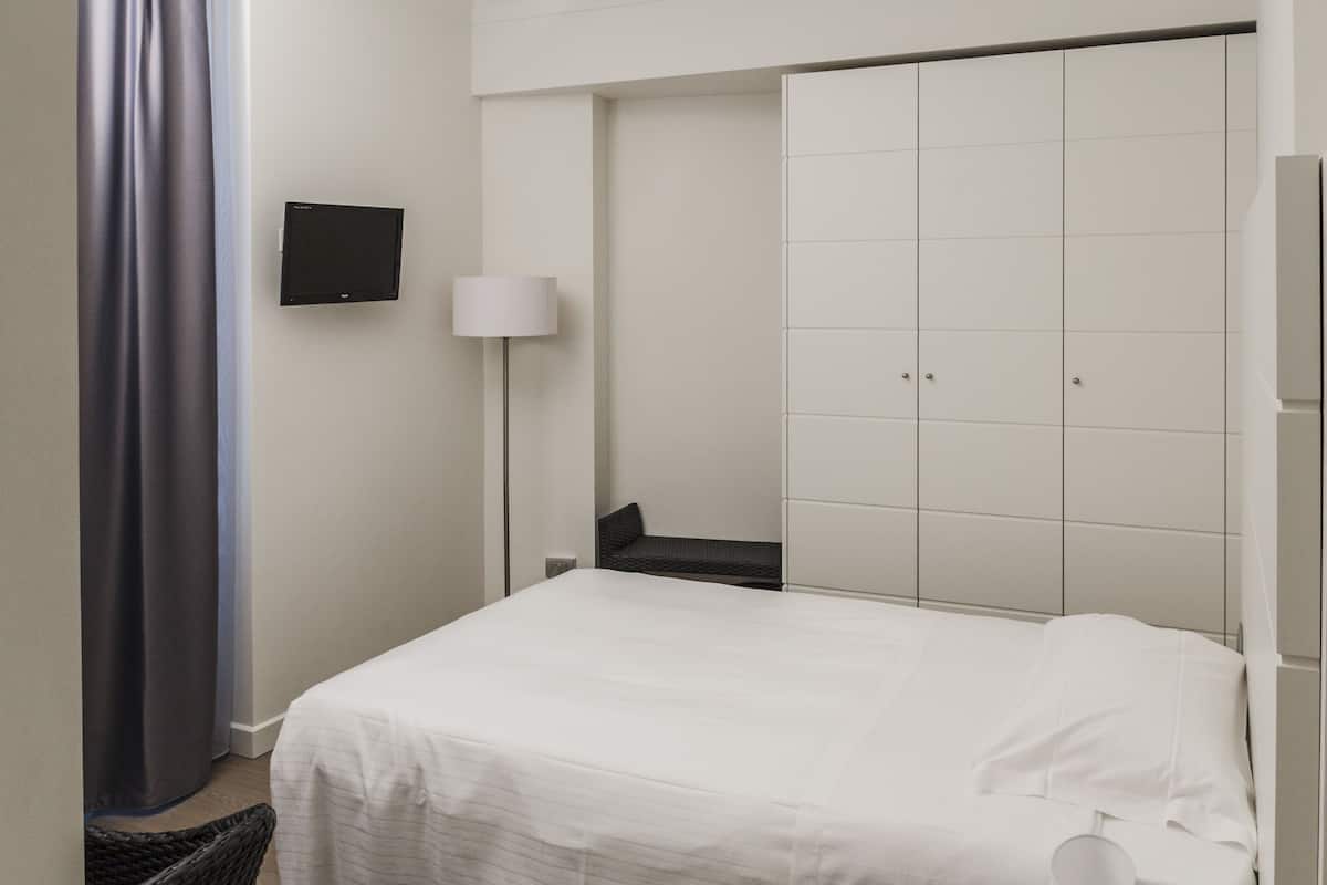 A hotel room with a bed, a television mounted on the wall, a bedside lamp, and a wardrobe with a mirror.