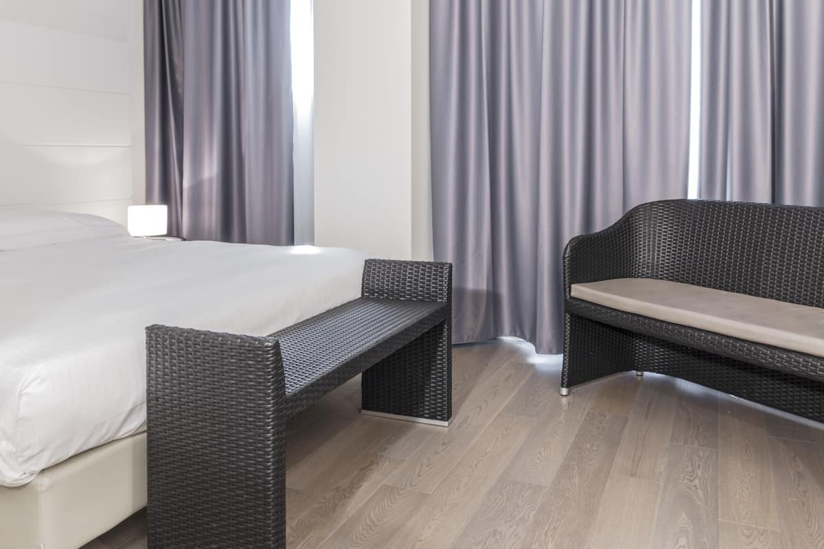 A hotel room with a bed, a bench, and a window with curtains.
