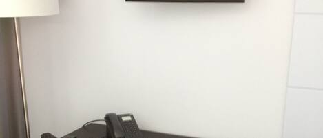 Habitación de hotel con una televisión de pantalla plana montada en la pared, un escritorio con teléfono y una silla con cojín.