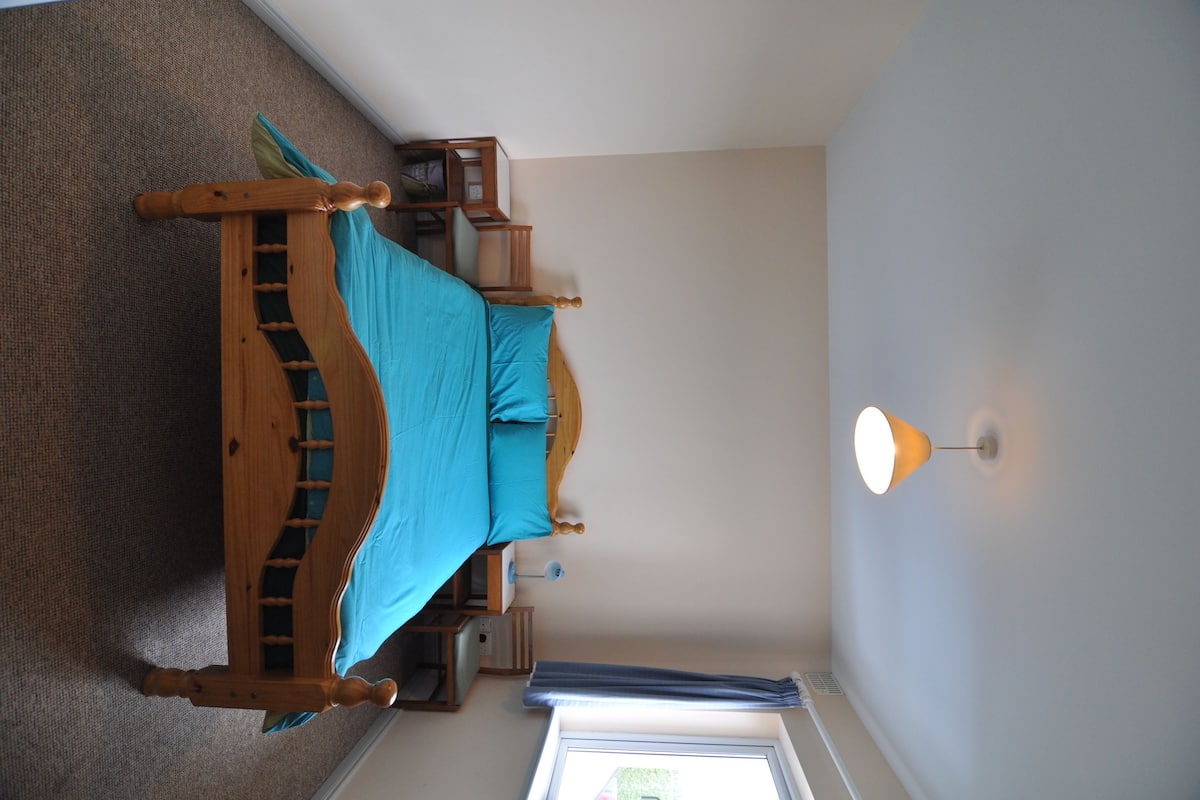 A bedroom with a wooden bed, a nightstand, a lamp, and a window with curtains.