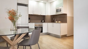 A modern kitchen with white cabinets, a glass table, and a vase with flowers. - Feelathome Plaza Apartments (Barcelona)