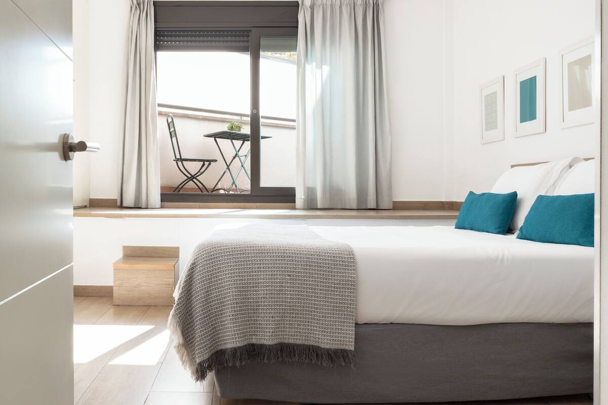 Een slaapkamer met een bed, een balkon met een tafel en stoelen, en uitzicht op de omgeving.