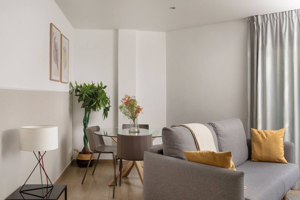 Een moderne woonkamer met een grijze bank, een eettafel en een potplant.