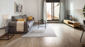 A modern living room with a sofa, a coffee table, a TV stand, and a view to the outside. - Feelathome Plaza Apartments (Barcelona)