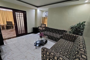 A living room with a patterned sofa, a coffee table, and a potted plant. - Manila Crown Palace Hotel (Manila)