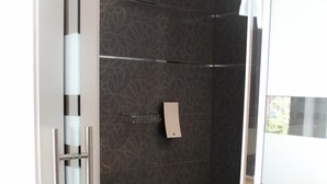 Un baño moderno con cabina de ducha de vidrio, baldosas oscuras con diseño y un toallero visible.