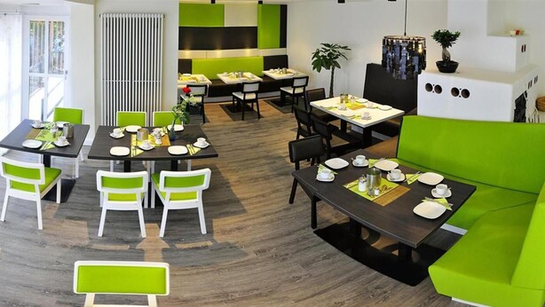 Un comedor moderno con sillas verdes y blancas, mesas negras y un sofá verde.