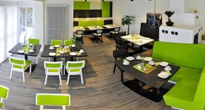 Un espace de repas moderne avec des chaises vertes et blanches, des tables noires et un canapé vert.