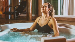 Una persona relajándose en un jacuzzi con una terraza de madera y sillas al fondo.