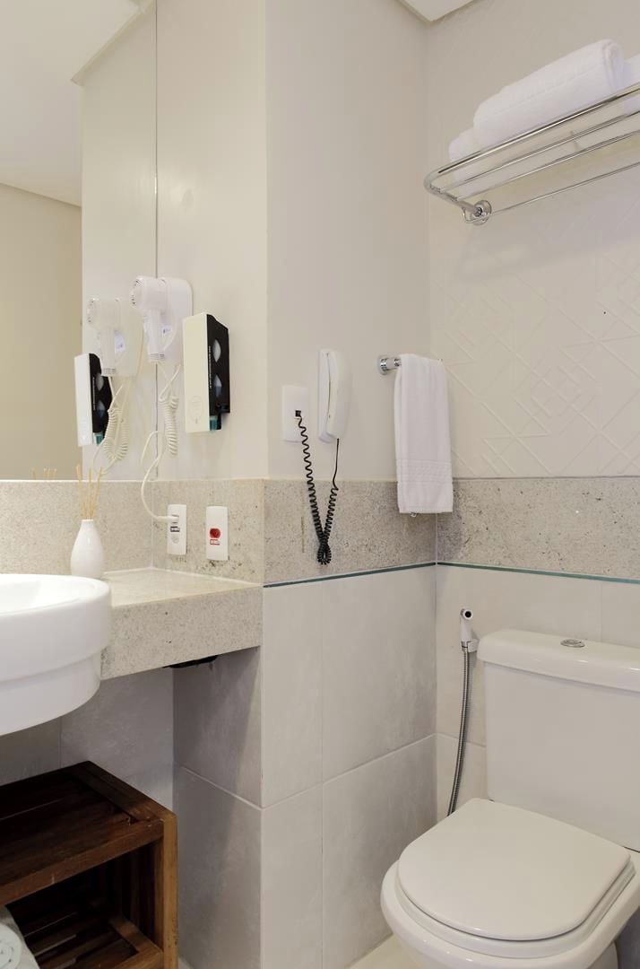 A bathroom with a white sink, a mirror, a toilet, a towel rack, and a shower area.