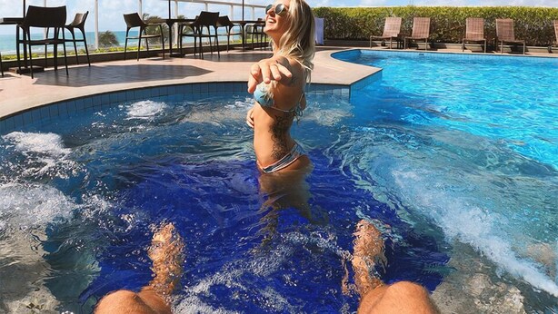 Zona de piscina con sillones de descanso y sombrillas, cielo despejado y vista al océano.