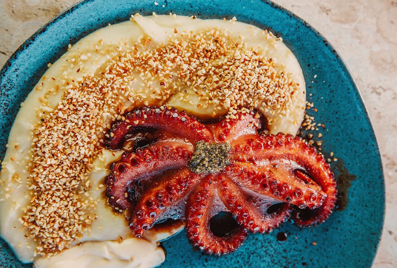A plate with octopus and a creamy dish, garnished with sesame seeds.