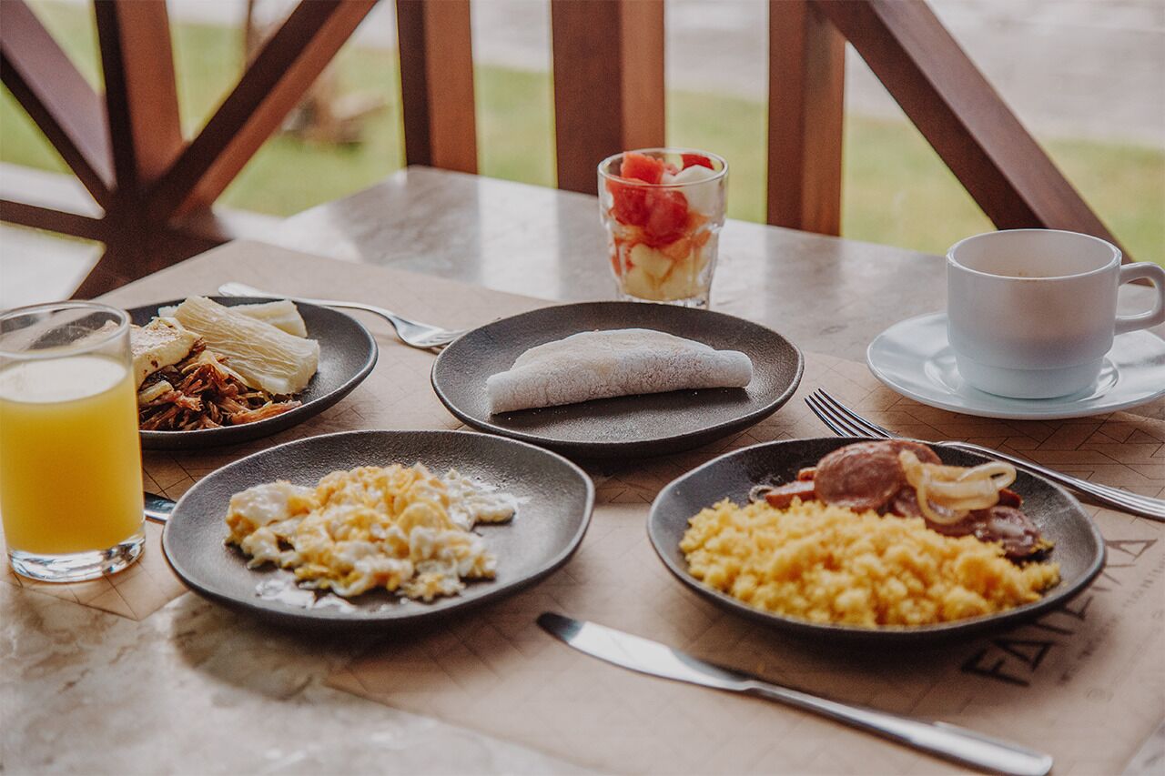 Ett frukostbord med tallrikar fyllda med rörägg, en rullad bakelse, en fruktsallad och en kopp kaffe.