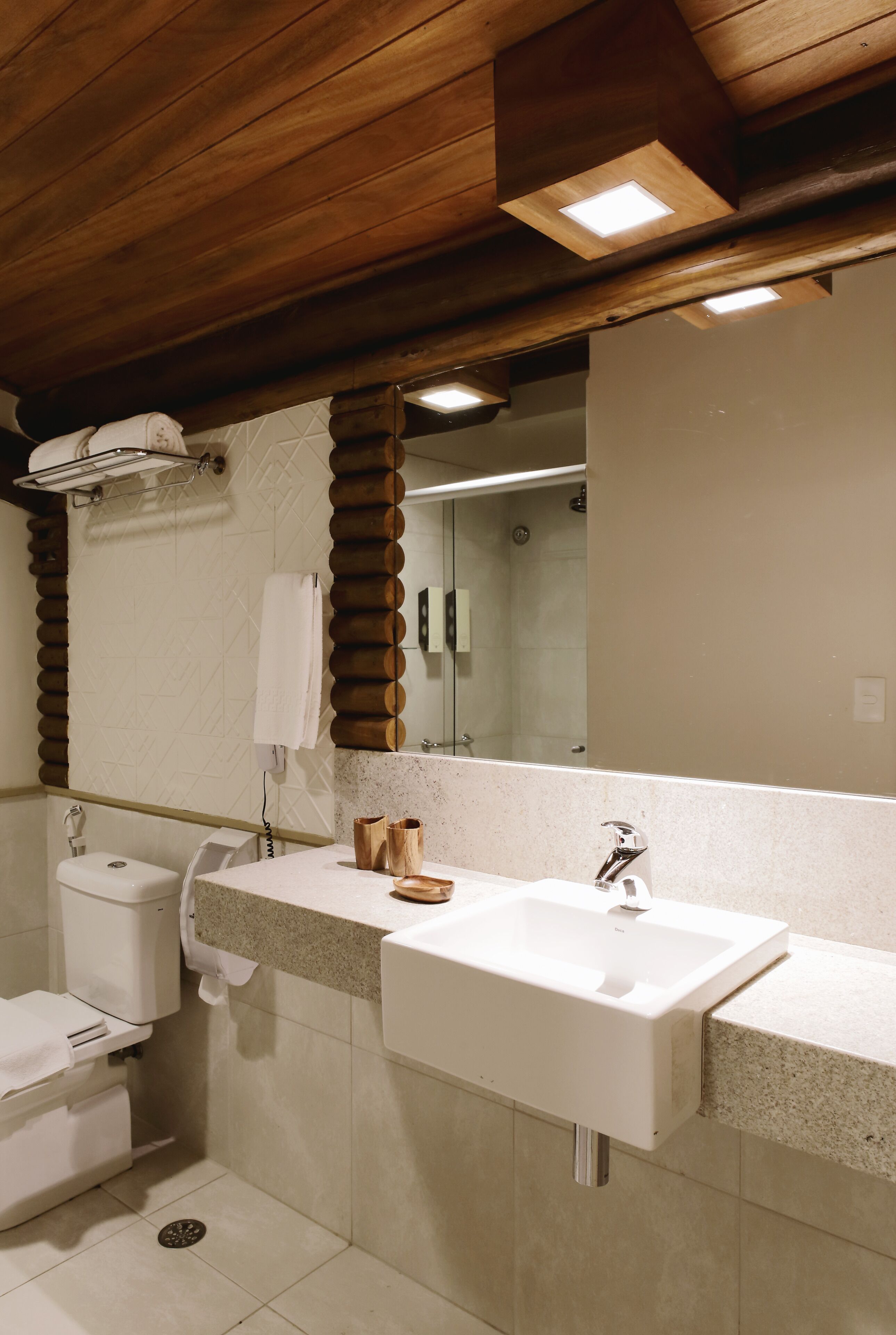 A modern bathroom with a wooden ceiling, a large mirror, a sink, and a toilet.