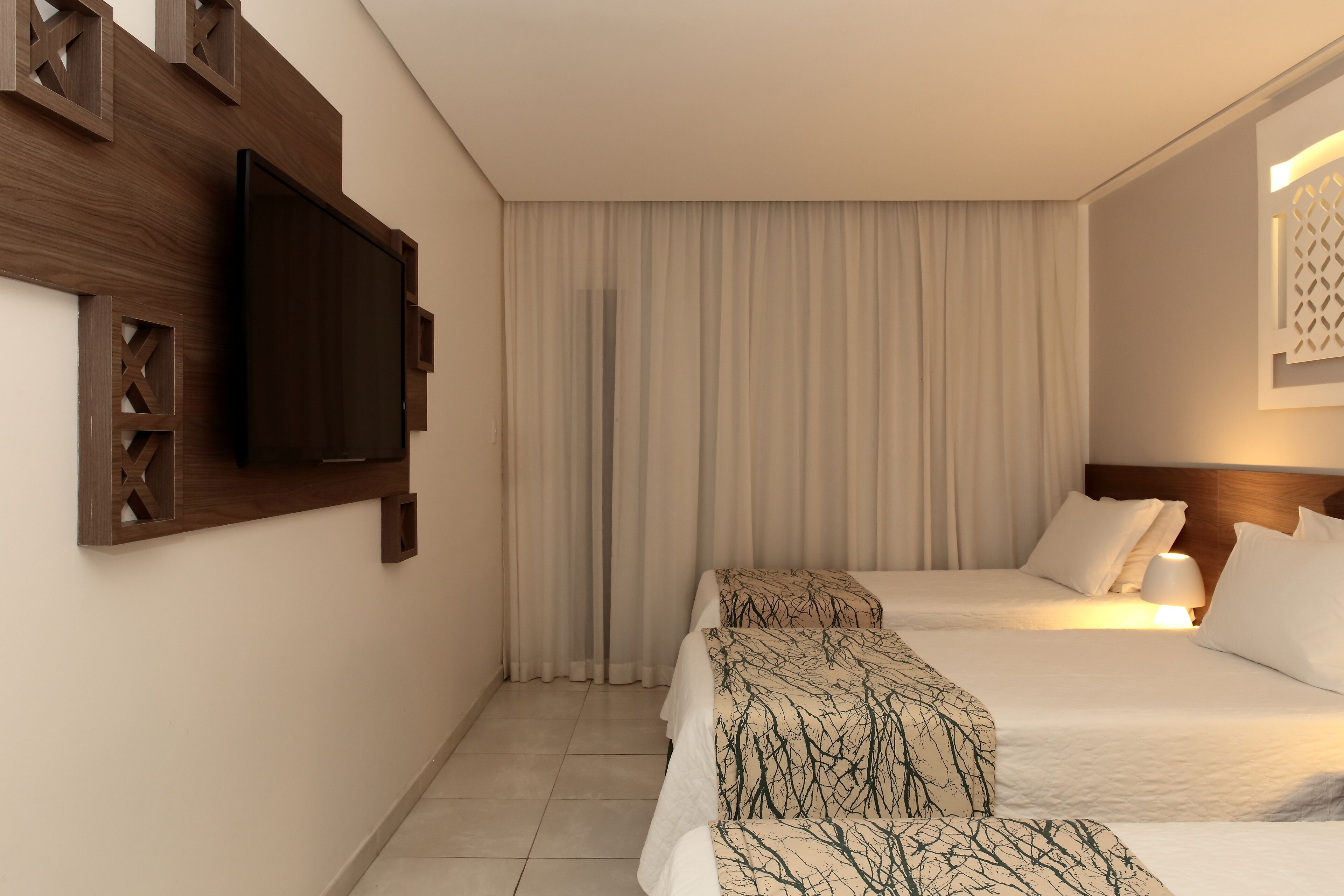 A hotel room with two beds, a flat-screen TV mounted on the wall, and a large window with curtains.