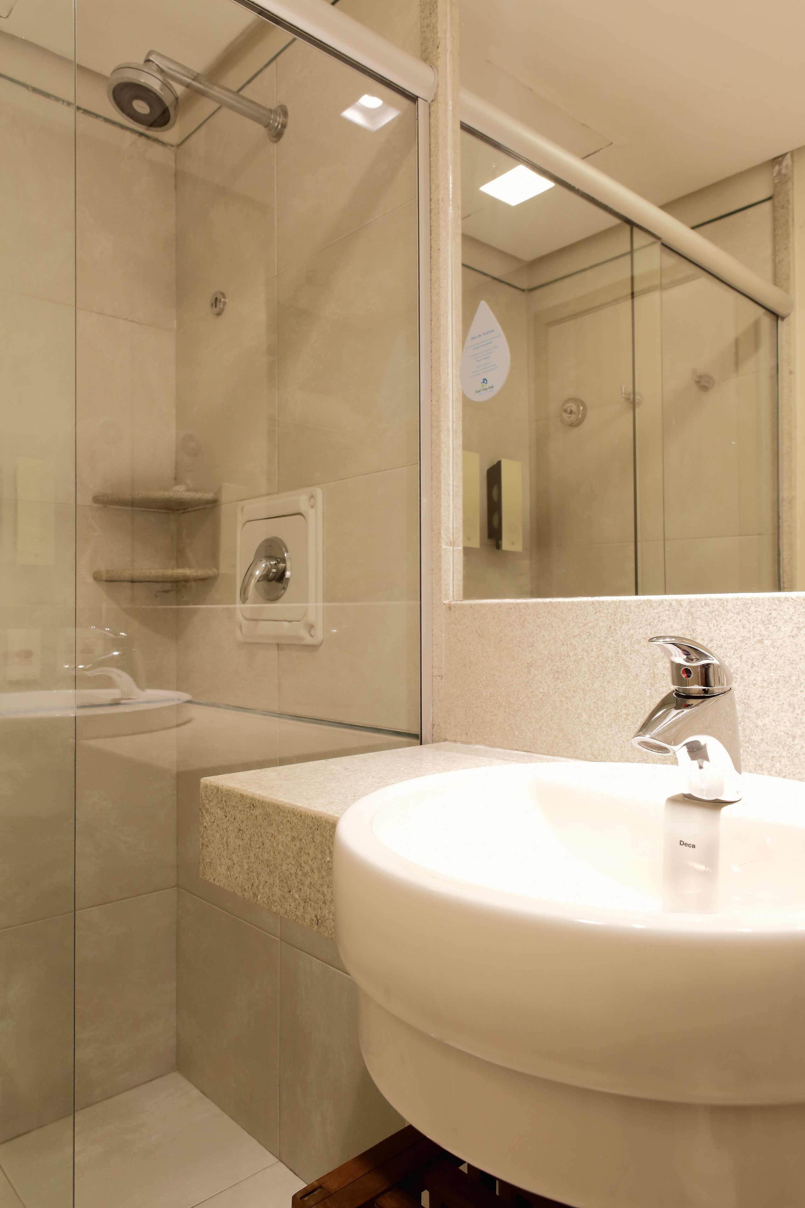 Een moderne badkamer met een douchecabine van glas, een wastafel met een chromen kraan en een spiegel die de ruimte weerspiegelt.