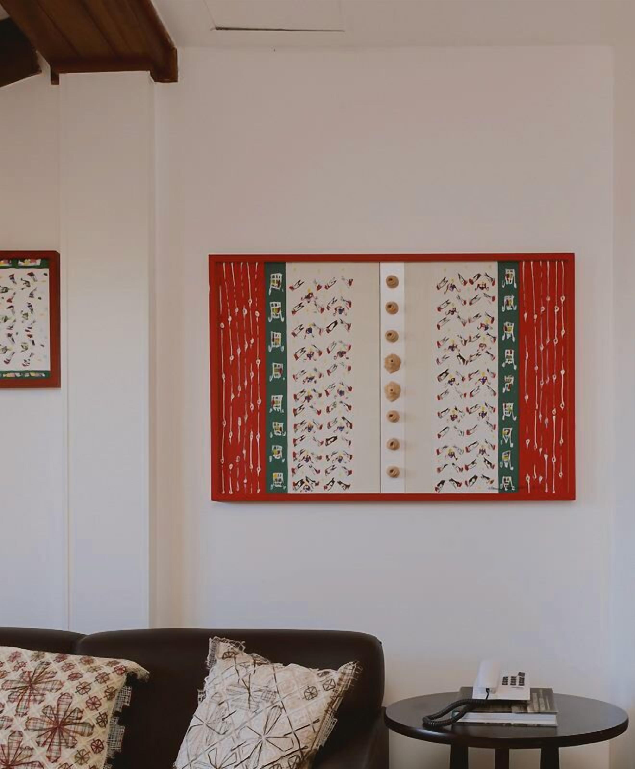 A room with a large wall-mounted artwork featuring a red and green color scheme with patterns and text.
