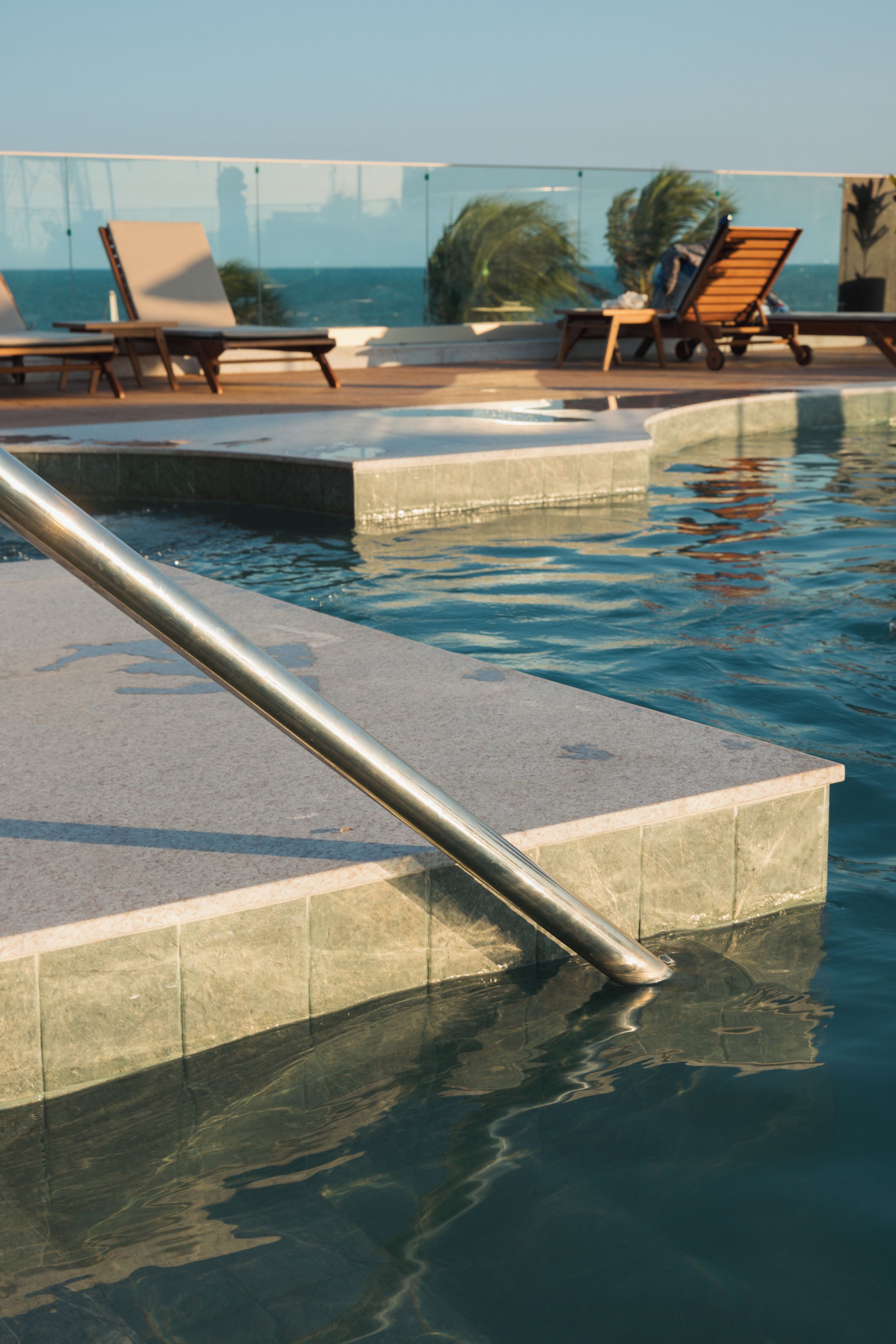A swimming pool with a metal handrail and lounge chairs.