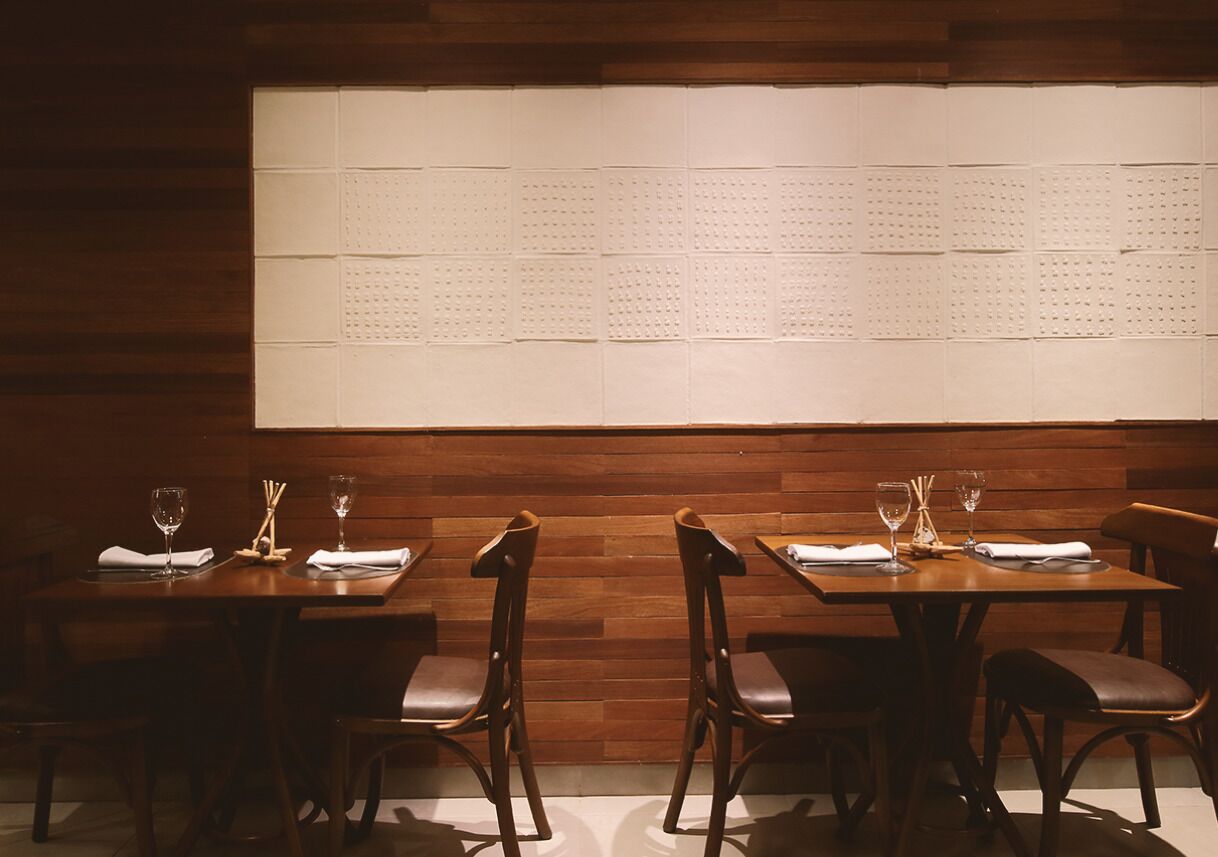 A restaurant interior with wooden panel walls, tables set with wine glasses and napkins, and chairs with leather seats.