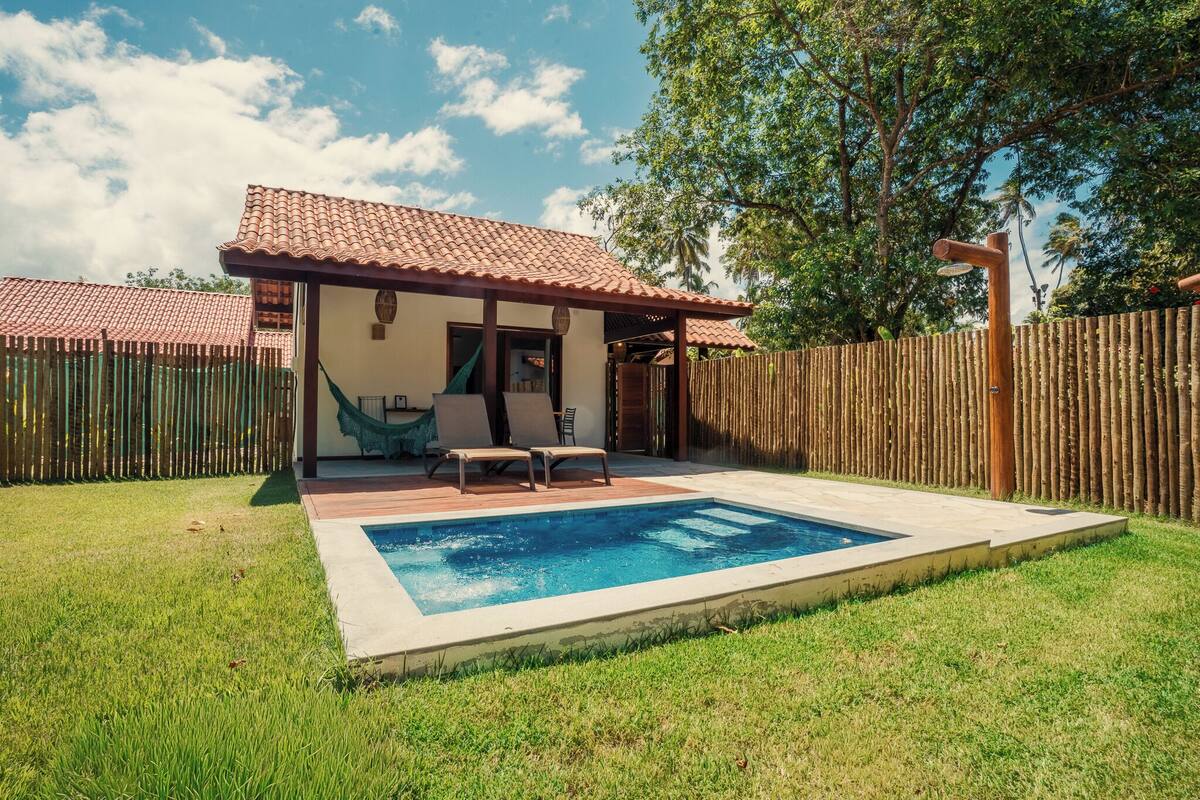 Une maison avec une piscine, un hamac et une clôture en bois.