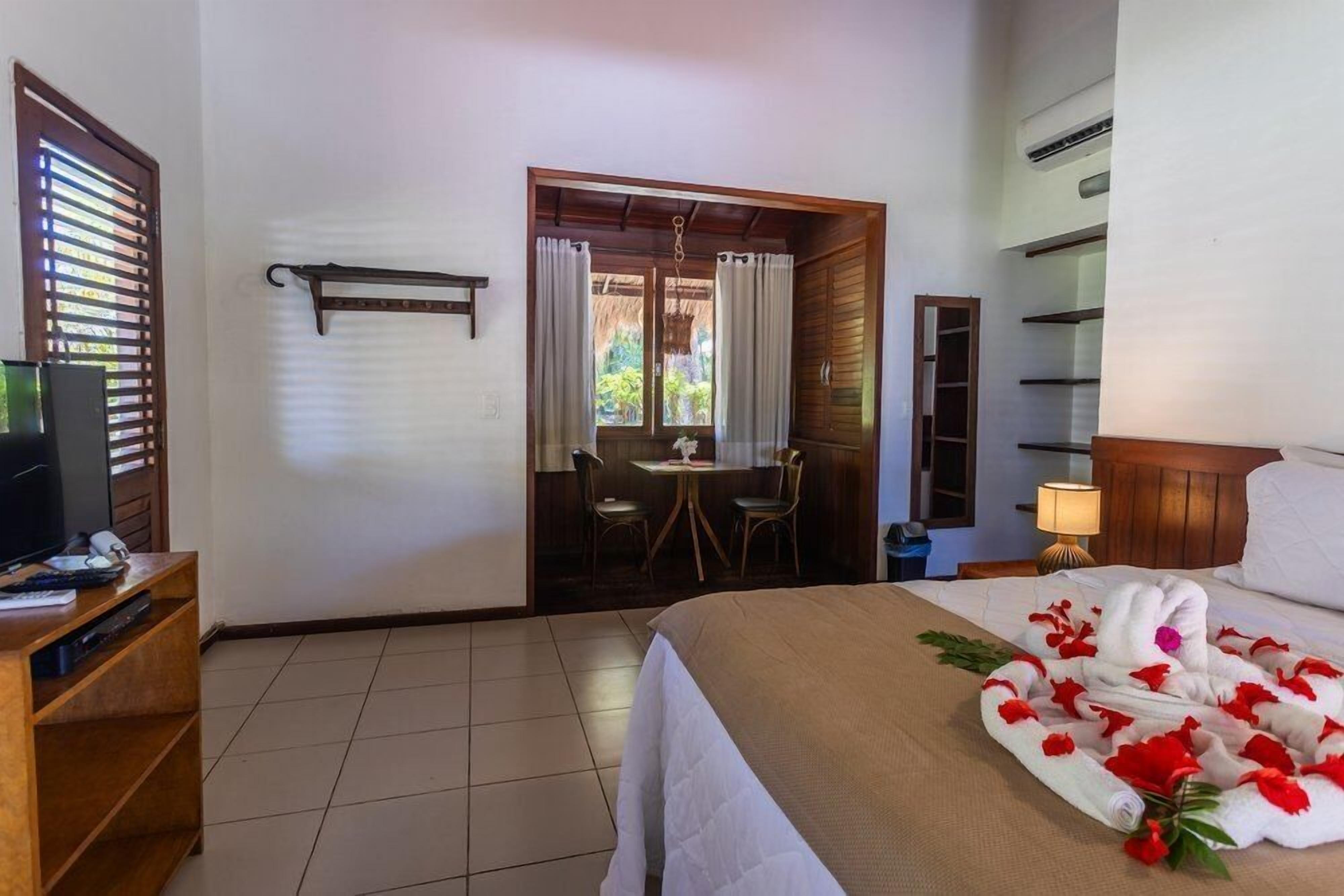 A hotel room with a bed, a desk, a TV, a small table with chairs, and a window with curtains.